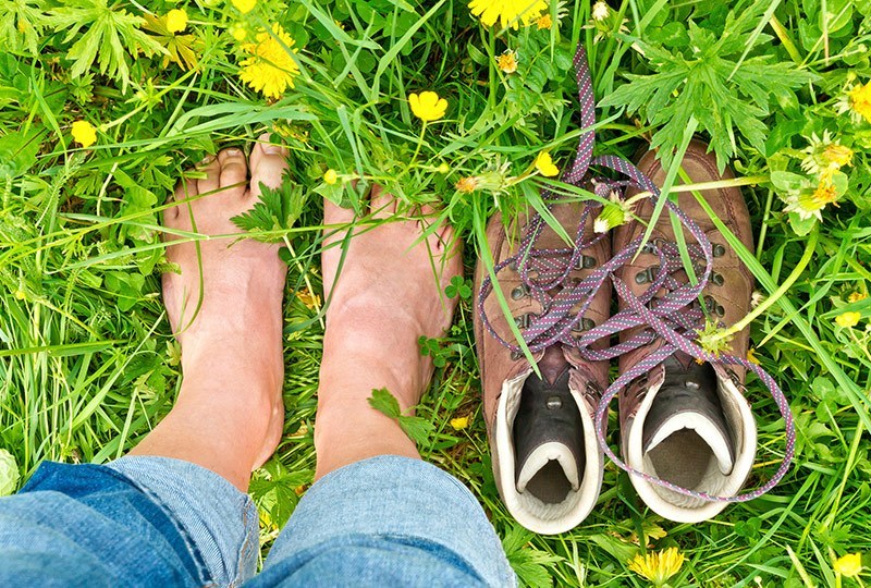 Nackte Füße im Gras, daneben Schuhe, die mit modernster Einlagetechnik ausgestattet sind.