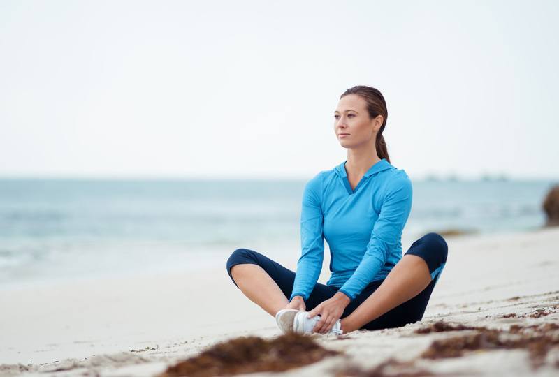 Eine Frau in Sportkleidung entspannt aktiv am Meer – dank Sport- und Massageprodukten.