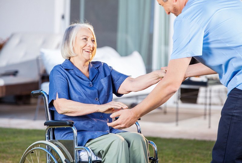 Eine alte Dame im Rollstuhl wird von einem Pfleger umsorgt.